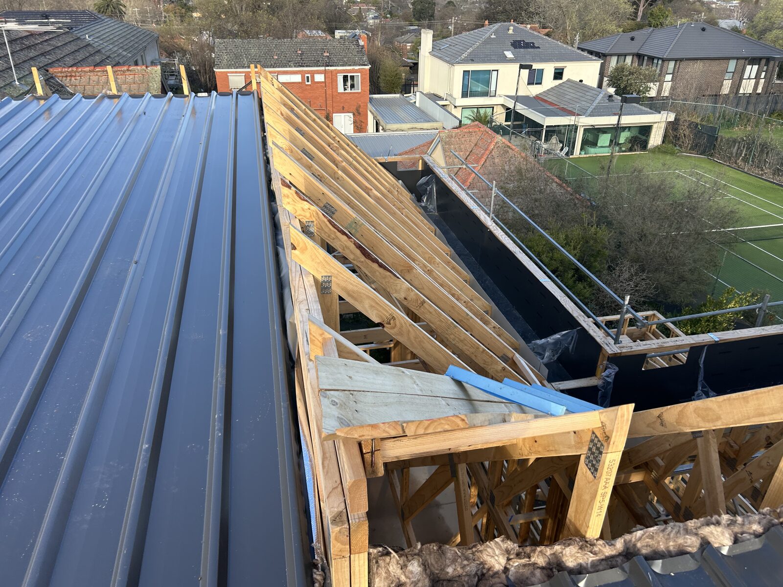 New dark metal roof sheets laid beside open timber trusses