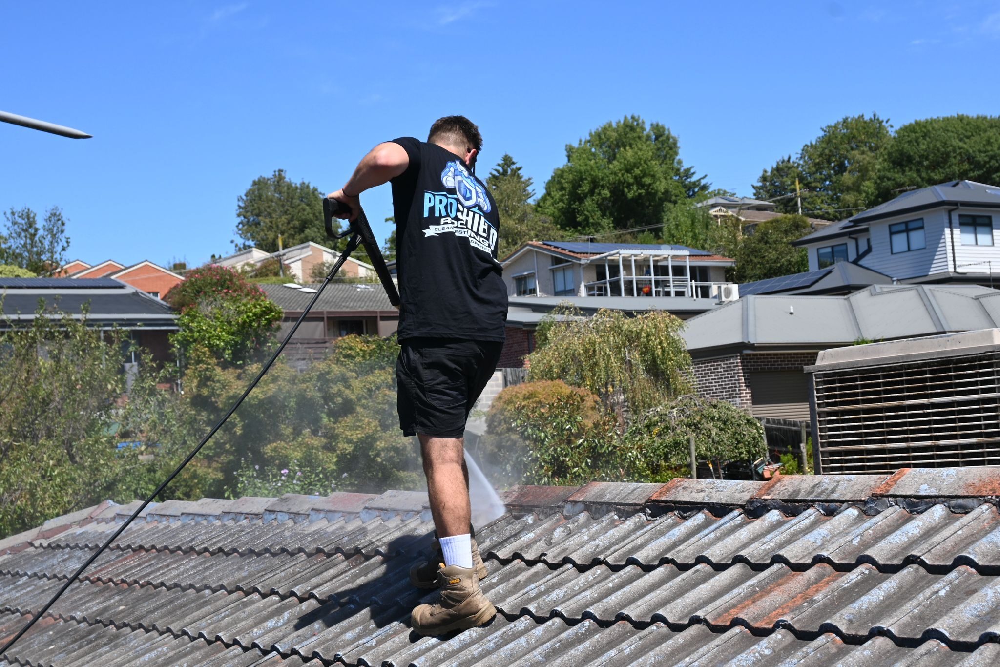 A Pro Shield roofer pressure washing a cement tile roof