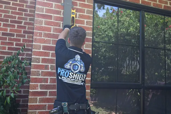 A Pro Shield roofer holding a level against a downpipe