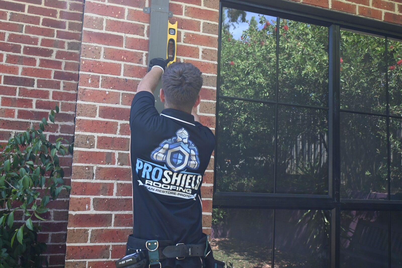 A Pro Shield roofer holding a level against a downpipe on a brick home