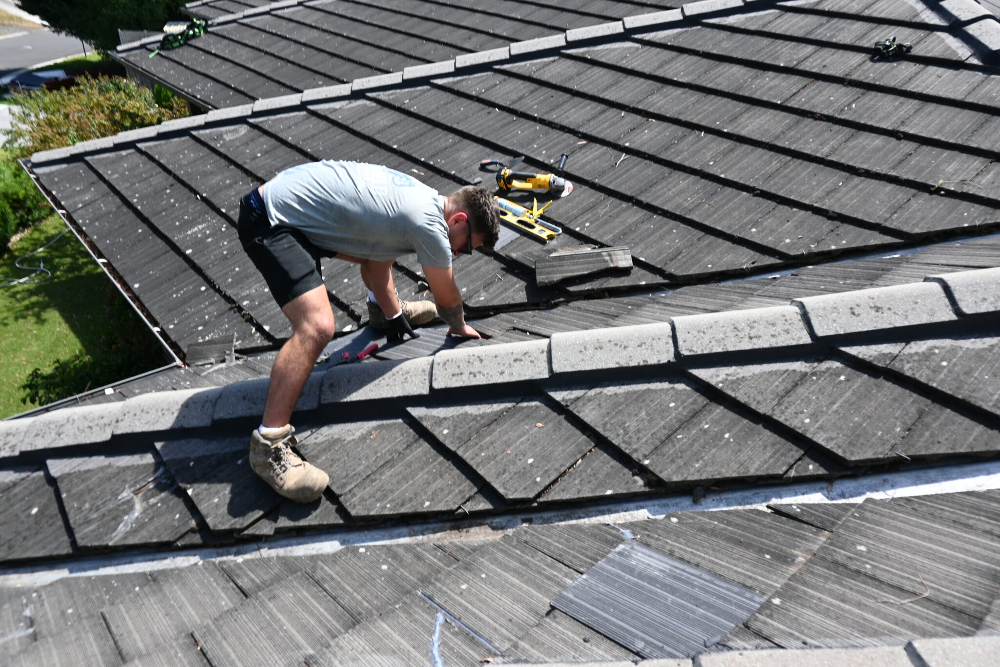 A roofer swapping out a tile beside the hip on a cement tile roof